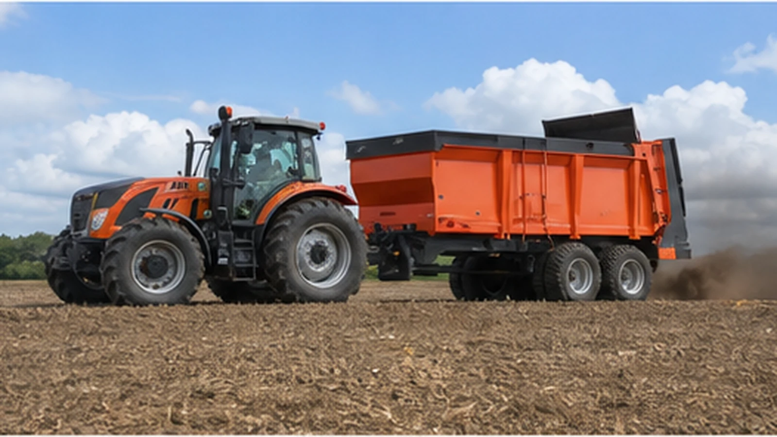Tractor pulling an orange farm transport trailer across a prepared field